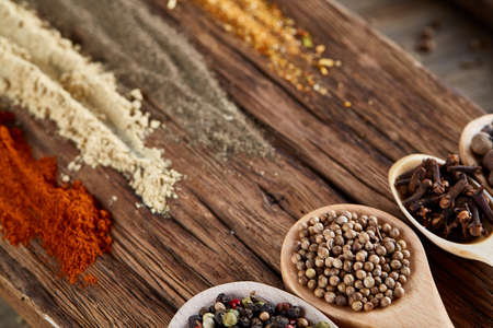 Row of wooden spoons with spices on vintage background, diminishing perspective, close-up, selective focus. Flat wooden spoons full of pepper seeds, clove, coriander, cumin and allspice on vintage wooden background. Healthy eating concept.の写真素材