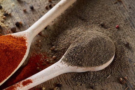 Top view of a wooden spoons full of paprica and black pepper on wooden barrel background, selective...