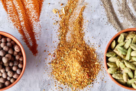 Green cardamon in ceramic bowl among ground scattered spicies on white textured background close-up, top view, selective focus. Exotic indian spice. Aromatic condiment. Healthy eating and dieting concept.の写真素材