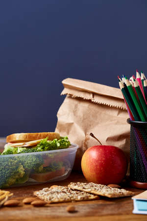 Concept of school lunch break with healthy lunch box full of sandwiches, apples and school supplies on white desk, selective focus. There is copy notepad and two markers, emphesizing the concept. Time for study and relax.の写真素材