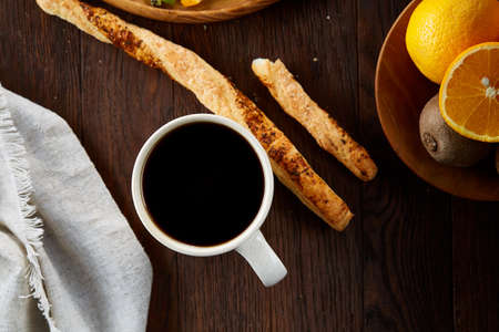 Morning concept with a cup of hot coffee, crispy breadsticks, and fresh oranges on wooden...