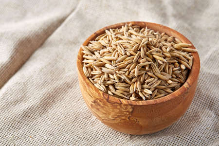 Oat groats or oat spike in wooden plate on homespun tablecloth, copy space, top view, selective focus. Healthy eating, dieting. Natural nutritious oatmeal. Vegan cuisine. Organic food concept.の写真素材