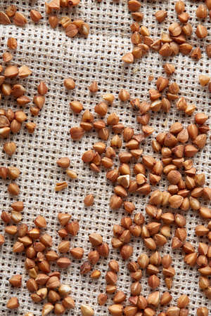 Buckwheat groats on burlap background, top view, close-up, selective focus, shallow depth of field, vertical. Buckwheat background. Useful natural cereal. Organic garnish. Premium cereal for healthy eating or dieting. Healthy food concept.の写真素材