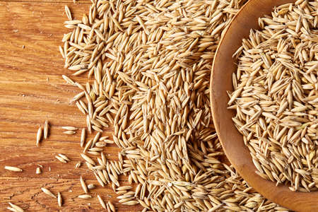 Pile of unpeeled oat grains on wooden background, top view, close-up, macro, selective focus, shallow depth of field. Some copy space. Dietary food. Healthy eating, dieting. Natural nutritious oatmeal. Vegan cuisine. Organic food concept.の写真素材