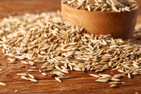Pile of unpeeled oat grains on wooden background, top view, close-up, macro, selective focus, shallow depth of field. Some copy space. Dietary food. Healthy eating, dieting. Natural nutritious oatmeal. Vegan cuisine. Organic food concept.の写真素材