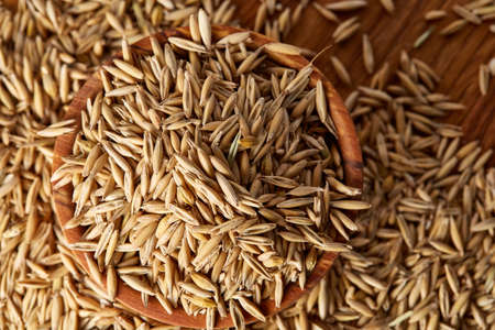 Pile of unpeeled oat grains on wooden background, top view, close-up, macro, selective focus, shallow depth of field. Some copy space. Dietary food. Healthy eating, dieting. Natural nutritious oatmeal. Vegan cuisine. Organic food concept.の写真素材