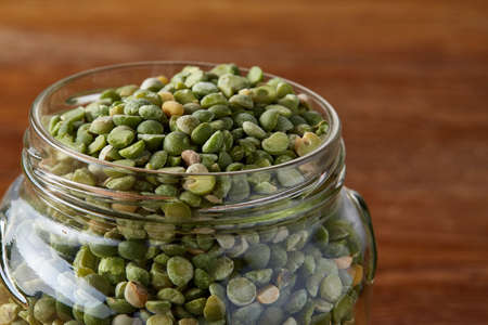Raw green peas in glass jar over wooden background, close-up, selective focus. Some copy space for your inscription. Organic protein. Perfect ingredient for vegan cuisine. Healthy food concept. Healthy eating, dieting.の写真素材