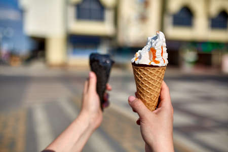 A first person view, girl walking along the road, holding ice cream in her hands and eating it in...
