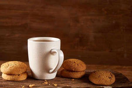 White porcelain mug of black tea or earl grey and pile of sweet cookies on flat piece of wood over rustic wooden background, top view, selective focus. Studio shot. Morning concept. Healthy eating concept.の写真素材