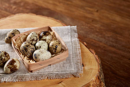 Composition of quail eggs box, eggs on a homespun napkin on a round log over wooden background,...