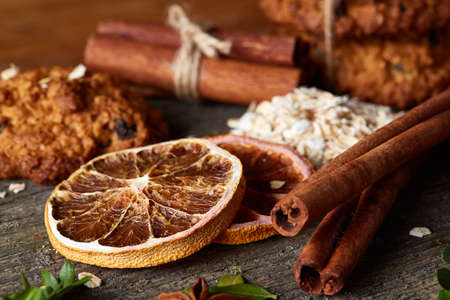 Christmas composition with sweet chocolate biscuits tied up with a ribbon, cinnamon sticks and dried oranges on rustic wooden background, close-up. Festive concept. Christmas background. Seasonal still life. Traditional Xmas composition.の写真素材