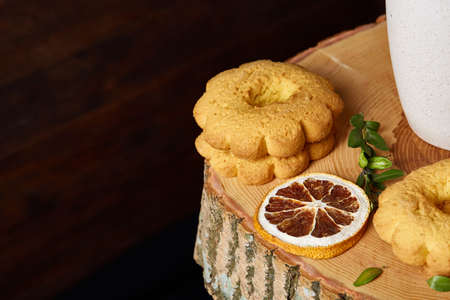 Christmas concept with a cup of hot tea, a large set of cookies, cinnamon sticks bunch, a couple of dried oranges, anise star and a branch of a spruce tree on a round log over rustic wooden background, selective focus.の写真素材