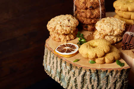 Conceptual composition with assortment of cookies, cinnamon sticks bunch and dried oranges on a wooden barrel over rustic background, selective focus, close-up. Delicious treat. Relaxing teatime. Christmas background.の写真素材
