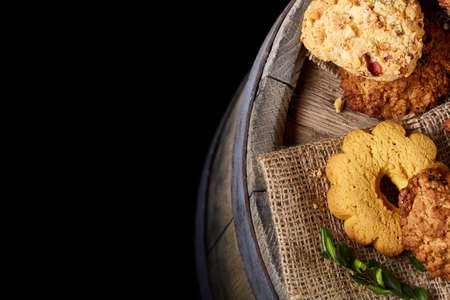 Conceptual composition with assortment of cookies, cinnamon sticks bunch and dried oranges on a wooden barrel over rustic background, selective focus, close-up. Delicious treat. Relaxing teatime. Christmas background.の写真素材