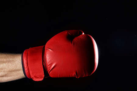 A fighter's red boxing gloves on his hand isolated over dark blurred background. Close-up of the muscular man's hands with blue boxing gloves, low key. Getting redy for fight. Athletic bodyparts. Sports background. Healthy lifestyle concept.の写真素材