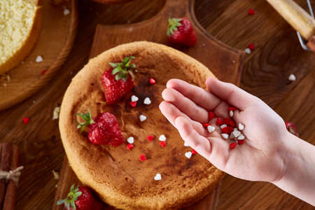 Close up of girl's hands decorating top of delicious strawberry cake, close up, selective focus....