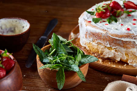 Strawberry tart covered with whipped sour cream on a wooden tray over rustic background, close-up, selective focus, shallow depth of field. Homemade bakery with fresh eggs, mint leaves, organic strawberry and flour. Food concept. Bakery background.の写真素材