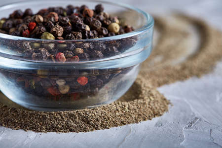 Black pepper corns in glass bowl on white background, top view, selective focus, vertical. Some copy...