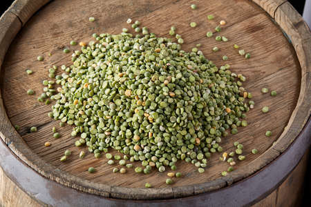 Pile of green peas on the top of wooden barrel, close-up, top view, selective focus.