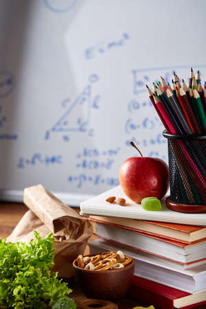Back to School concept, school supplies, assortment of biscuits and transparent lunchbox full of sandwich, fruits and vegetables togather with assortment of biscuits on wooden desk in front of white chalkboard, selective focus, close-up.の写真素材