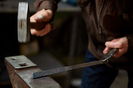 Close-up of a blacksmith's hands manipulating a metal piece above his forge in the smithy, selective...
