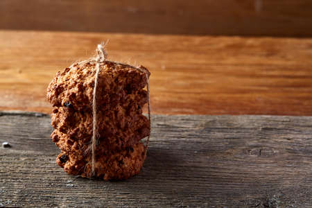 Bunch of chocolate biscuits tighted with a rope on a round wood log over rustic wooden background, close-up, selective focus. Bright gourmet sweetness. Freshly baked tasty cookies. Countryside background. Healthy eating concept.の写真素材