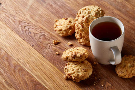 White porcelain mug of black tea or earl grey and pile of sweet cookies on rustic wooden background,...