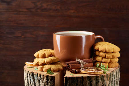 Christmas concept with a cup of hot tea, a large set of cookies, cinnamon sticks bunch, a couple of dried oranges, anise star and a branch of a spruce tree on a round log over rustic wooden background, selective focus.の写真素材