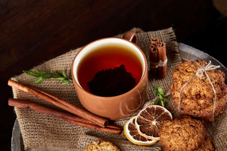Traditional Christmas tea concept with a cup of hot tea, a large set of cookies, cinnamon sticks bunch on a wooden background, selective focus, close-up. Delicious treat. Relaxing teatime. Christmas background. Festive concept.の写真素材