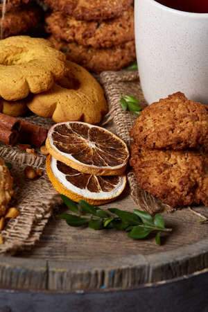 Traditional Christmas tea concept with a cup of hot tea, a large set of cookies, cinnamon sticks bunch on a wooden background, selective focus, close-up. Delicious treat. Relaxing teatime. Christmas background. Festive concept.の写真素材