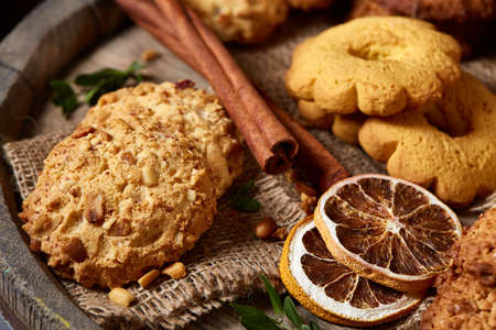 Conceptual composition with assortment of cookies, cinnamon sticks bunch and dried oranges on a wooden barrel over rustic background, selective focus, close-up. Delicious treat. Relaxing teatime. Christmas background.の写真素材