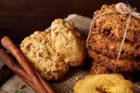Conceptual composition with assortment of cookies, cinnamon sticks bunch and dried oranges on a wooden barrel over rustic background, selective focus, close-up. Delicious treat. Relaxing teatime. Christmas background.の写真素材