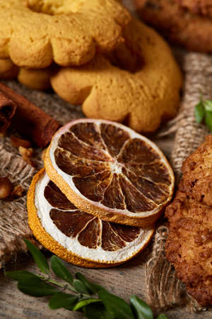 Conceptual composition with assortment of cookies, cinnamon sticks bunch and dried oranges on a wooden barrel over rustic background, selective focus, close-up. Delicious treat. Relaxing teatime. Christmas background.の写真素材