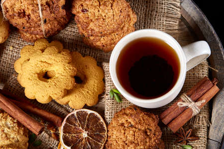 Traditional Christmas tea concept with a cup of hot tea, a large set of cookies, cinnamon sticks bunch on a wooden background, selective focus, close-up. Delicious treat. Relaxing teatime. Christmas background. Festive concept.の写真素材
