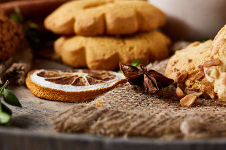 Conceptual composition with assortment of cookies, cinnamon sticks bunch and dried oranges on a wooden barrel over rustic background, selective focus, close-up. Delicious treat. Relaxing teatime. Christmas background.の写真素材