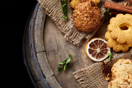 Conceptual composition with assortment of cookies, cinnamon sticks bunch and dried oranges on a wooden barrel over rustic background, selective focus, close-up. Delicious treat. Relaxing teatime. Christmas background.の写真素材