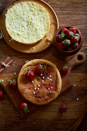 Delicious cake with fresh organic strawberries on cutting board over wooden background, top view, close-up, selctive focus. Sweet homemade dessert on wooden table. Rustic background. Tasty morning pastry. Homemade food concept.の写真素材