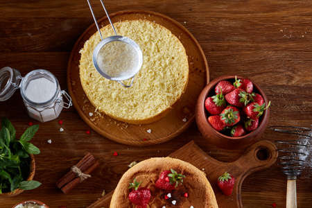 Delicious cake with fresh organic strawberries and mint, top view, close-up, selctive focus. Sweet homemade dessert surrounded by natural ingredients on wooden table. Rustic background. Tasty morning pastry. Homemade food concept.の写真素材