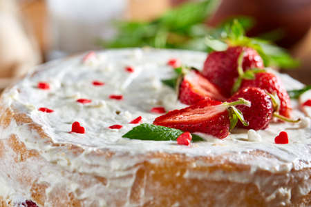 Strawberry tart covered with whipped sour cream surrounded by organic ingredients and kitchen utensils over wooden background, flat lay, selective focus. Homemade bakery with fresh mint leaves. Food concept. Bakery background.の写真素材