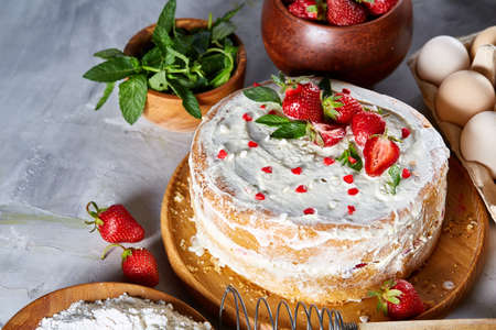 Strawberry tart covered with whipped sour cream surrounded by organic ingredients over white background, flat lay, selective focus. Homemade bakery with fresh eggs, mint leaves, organic strawberry and flour. Food concept. Bakery background.の写真素材