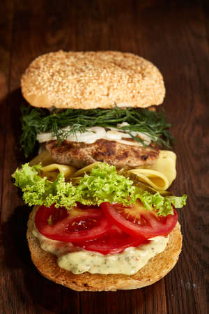 Close-up of delicious fresh home made burger with piccoli, lettuce, cheese, onion, tomato, dill and yummy beef on a dark wooden background, vertical. Traditional American hamburger. Junk food full of calories. Fast food concept.の写真素材