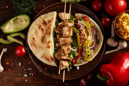 Exotic still slife with pita on an old-fashioned plate, fresh vegetables and yummy kebab over...