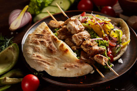 Exotic still slife with pita on an old-fashioned plate, fresh vegetables and yummy kebab over vintage wooden background, side view, close-up, shallow depth of field. Mediterranian or Middle East cuisine. Rustic food background. Fast food concept.の写真素材