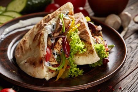 Exotic stuffed pita on an old-fashioned plate with fresh vegetables and beans over vintage wooden background, top view, close-up, selective focus. Mediterranian or Middle East cuisine. Rustic food background. Fast food concept.の写真素材