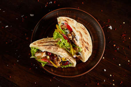 Tasty Jewish pita stuffed with grilled chicken, vegetables, beans, letucce and sauce on old-fashioned plate over vintage wooden background, top view, close-up, selective focus. Organic stuffed roll. Traditional Middle East cuisine. Fast food concept.の写真素材