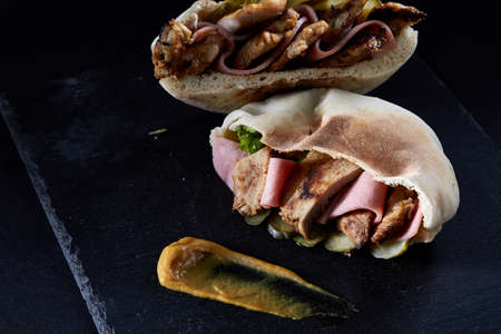 Stuffed pita bread with pork, ham, piccoli and sauce on black stony background, close-up, selective focus. Organic stuffed roll for delicious lunch. Traditional Middle East cuisine. Fast food concept.の写真素材