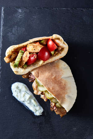 Stuffed pita bread with pork chops, grilled vegetables and sauce on black stony background, close-up, selective focus, vertical. Organic stuffed roll for delicious lunch. Traditional Middle East cuisine. Fast food concept.の写真素材