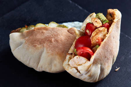 Stuffed pita bread with grilled vegetables and chiken chops on black stony background, close-up, selective focus. Organic stuffed roll for delicious lunch. Traditional Middle East cuisine. Fast food concept.の写真素材