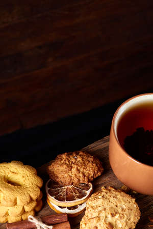 Sweet Christmas teatime with oatmeal, chocolate biscuits, cinnamon sticks and dried oranges, on rustic wooden background, close-up, selective focus. Christmas concept. Festive background.の写真素材