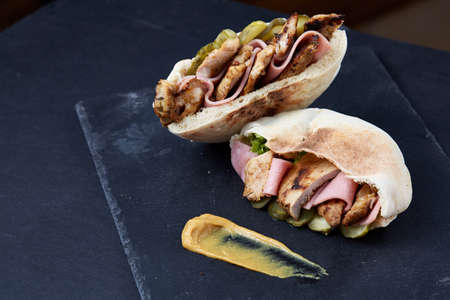 Stuffed pita bread with pork chops, grilled vegetables and sauce on black stony background, close-up, selective focus, vertical. Organic stuffed roll for delicious lunch. Traditional Middle East cuisine. Fast food concept.の写真素材
